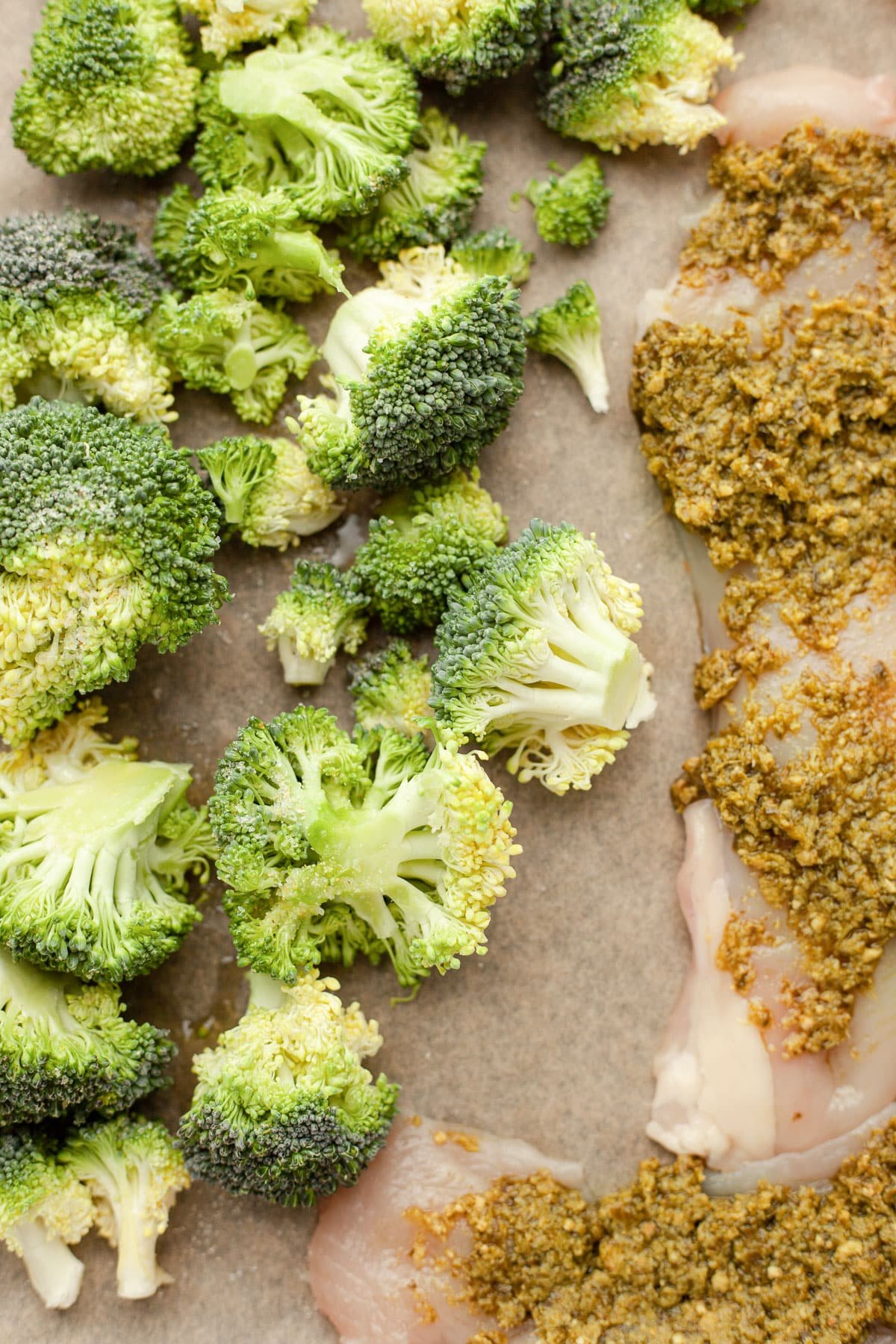 Chicken breasts covered in pesto sit on a baking sheet with broccoli.